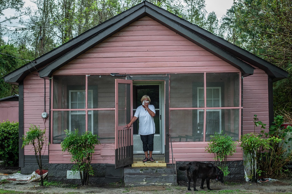 Activist Elsie Herring, stands on the porch of her family home, holding a handkerchief over her mouth to filter out manure being sprayed on the field next door.